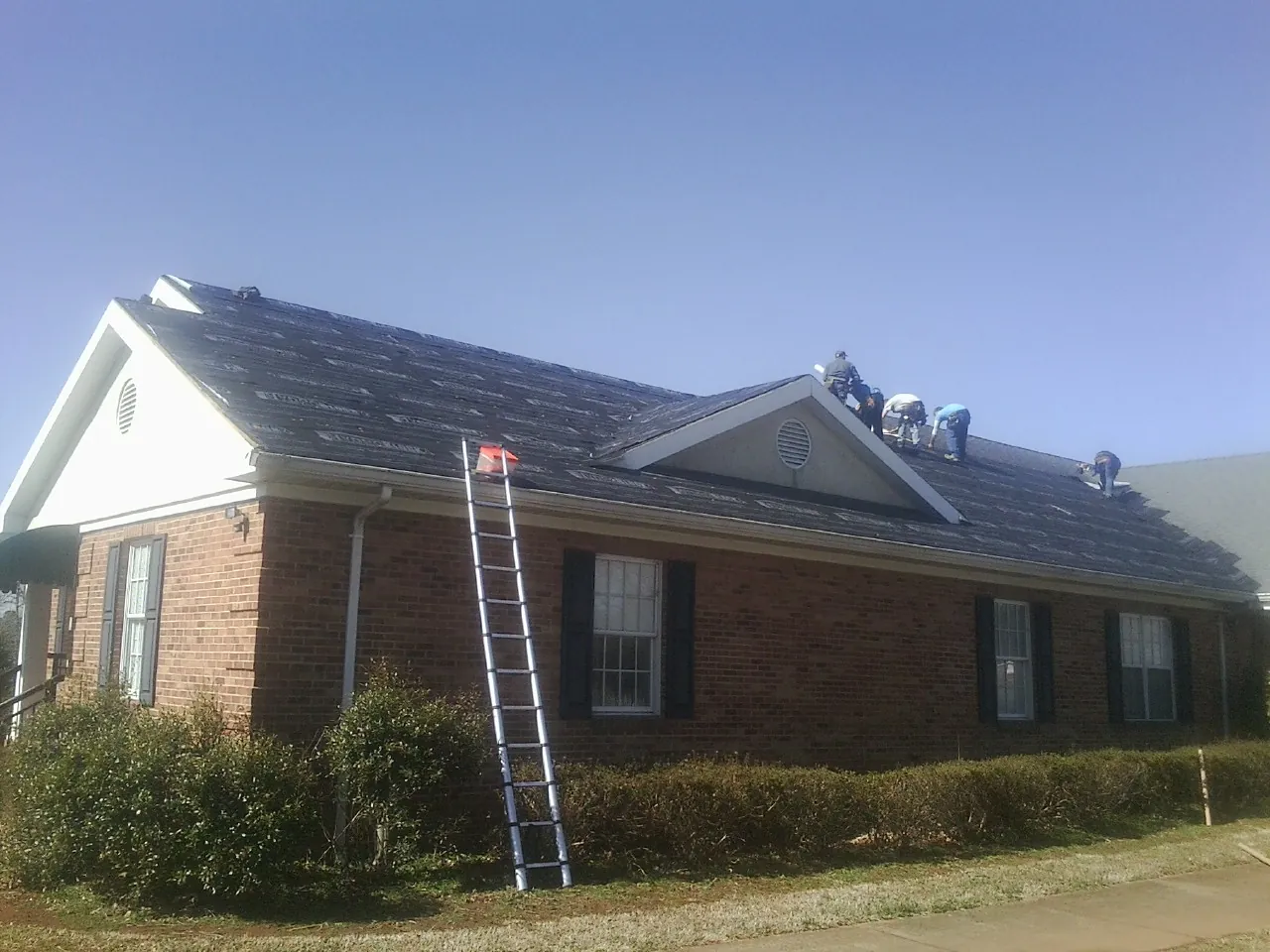 Crew tearing shingles off a brick ranch roof with a ladder set — Emergency Roof Repair work by our crew in Hunter