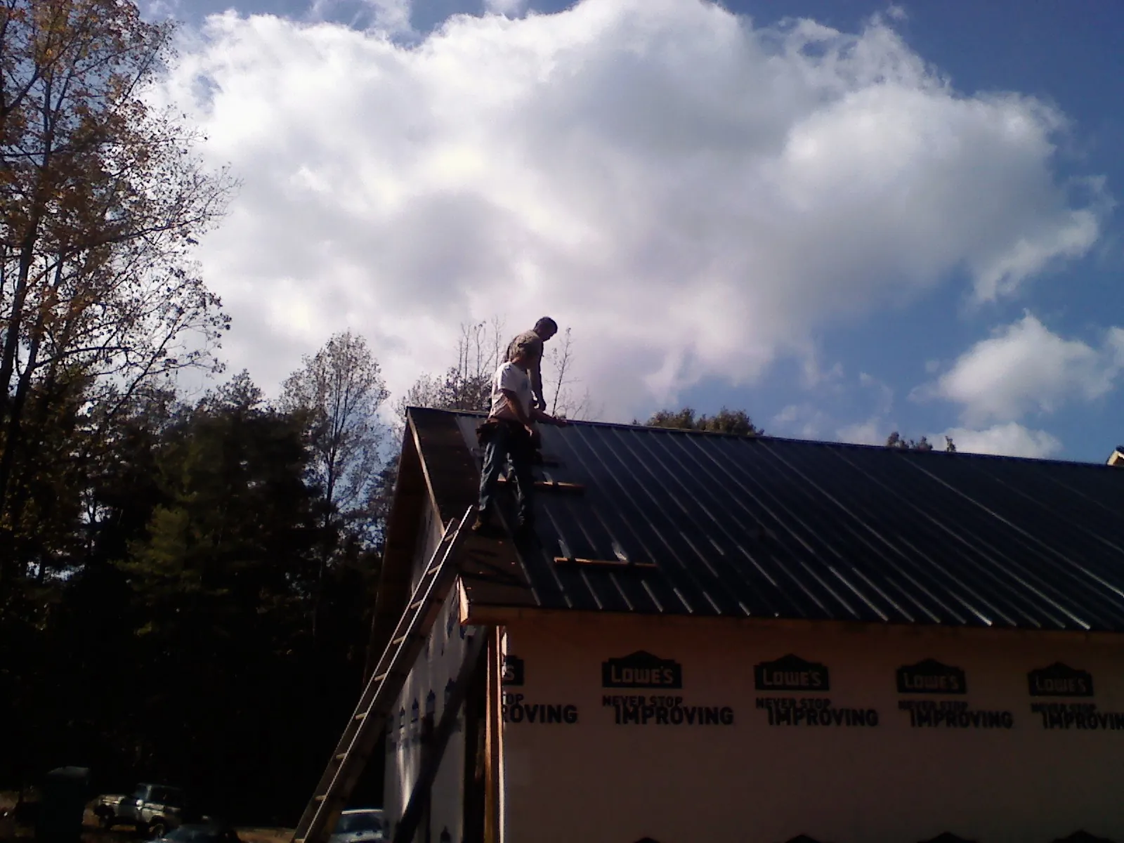 Roofer fastening dark metal panels high against a cloudy sky, from a Roof Inspection job in Hunter