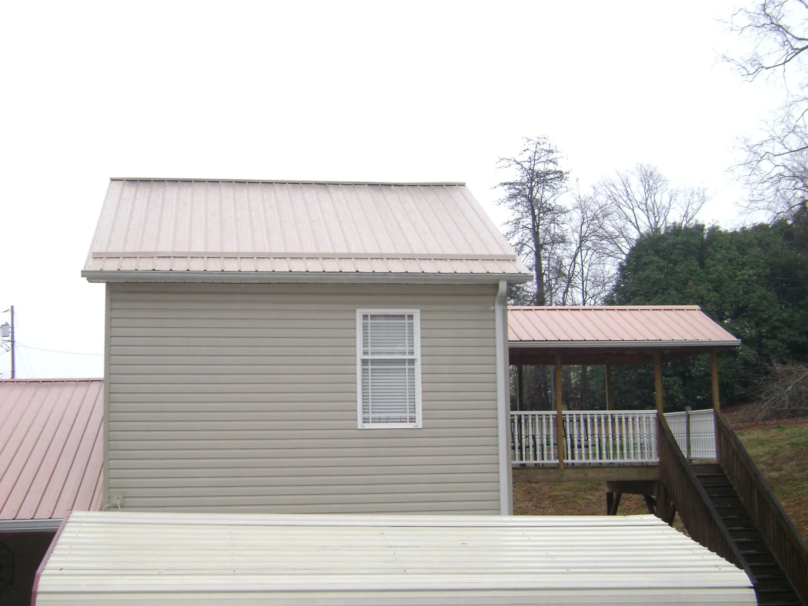 Tan metal roofs on a two story addition and attached porch, from a Roof Replacement job in Hunter